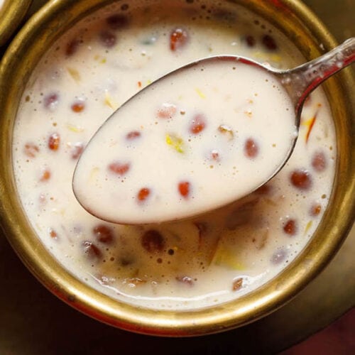 closeup shot of brass spoon filled with basundi on top of a brass bowl with basundi