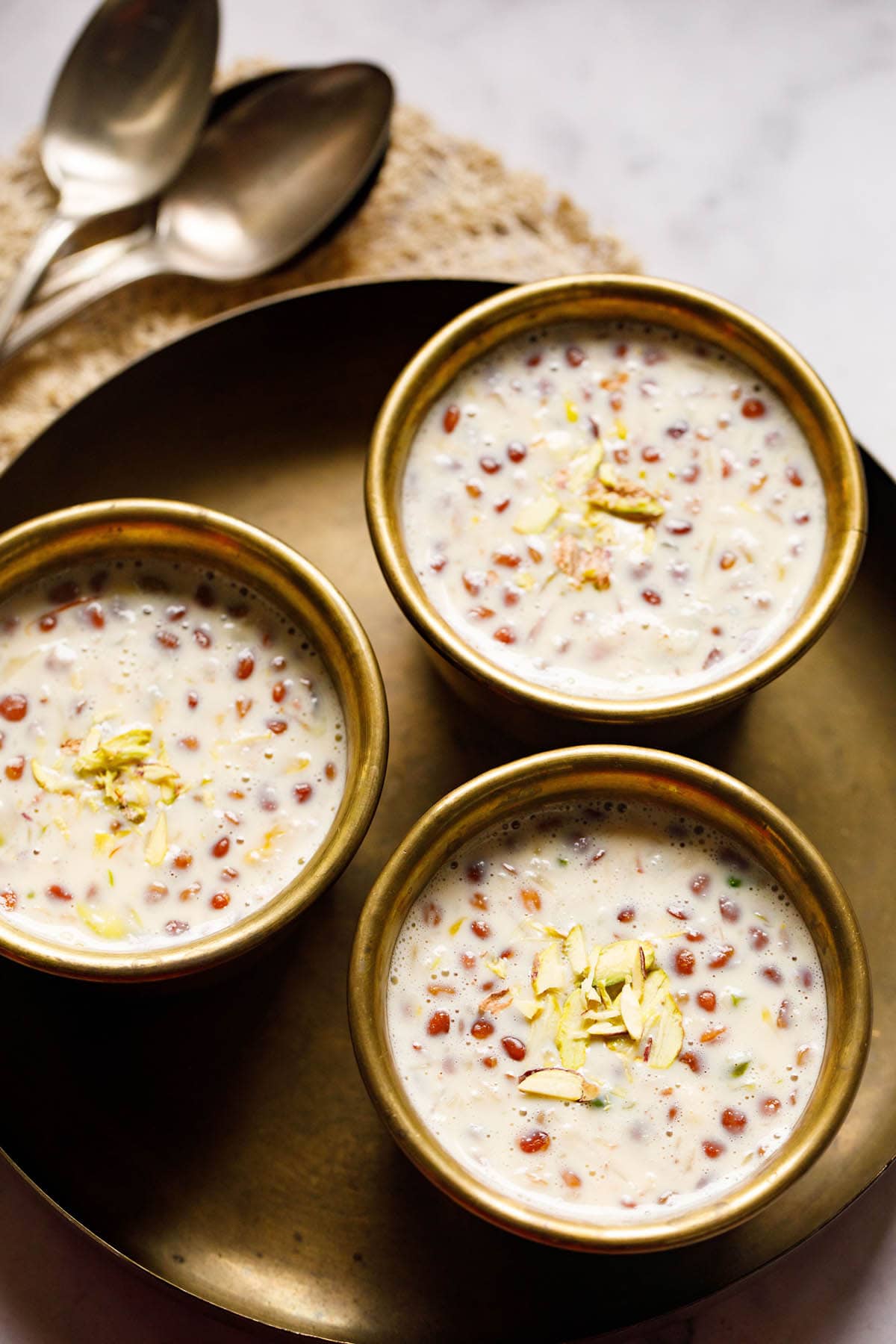 three brass bowls filled with basundi on a brass plate