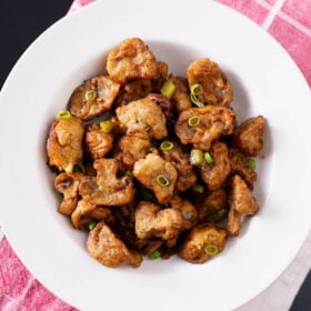 overhead shot of chilli mushroom in a shallow white bowl on a white and pink checkered napkin