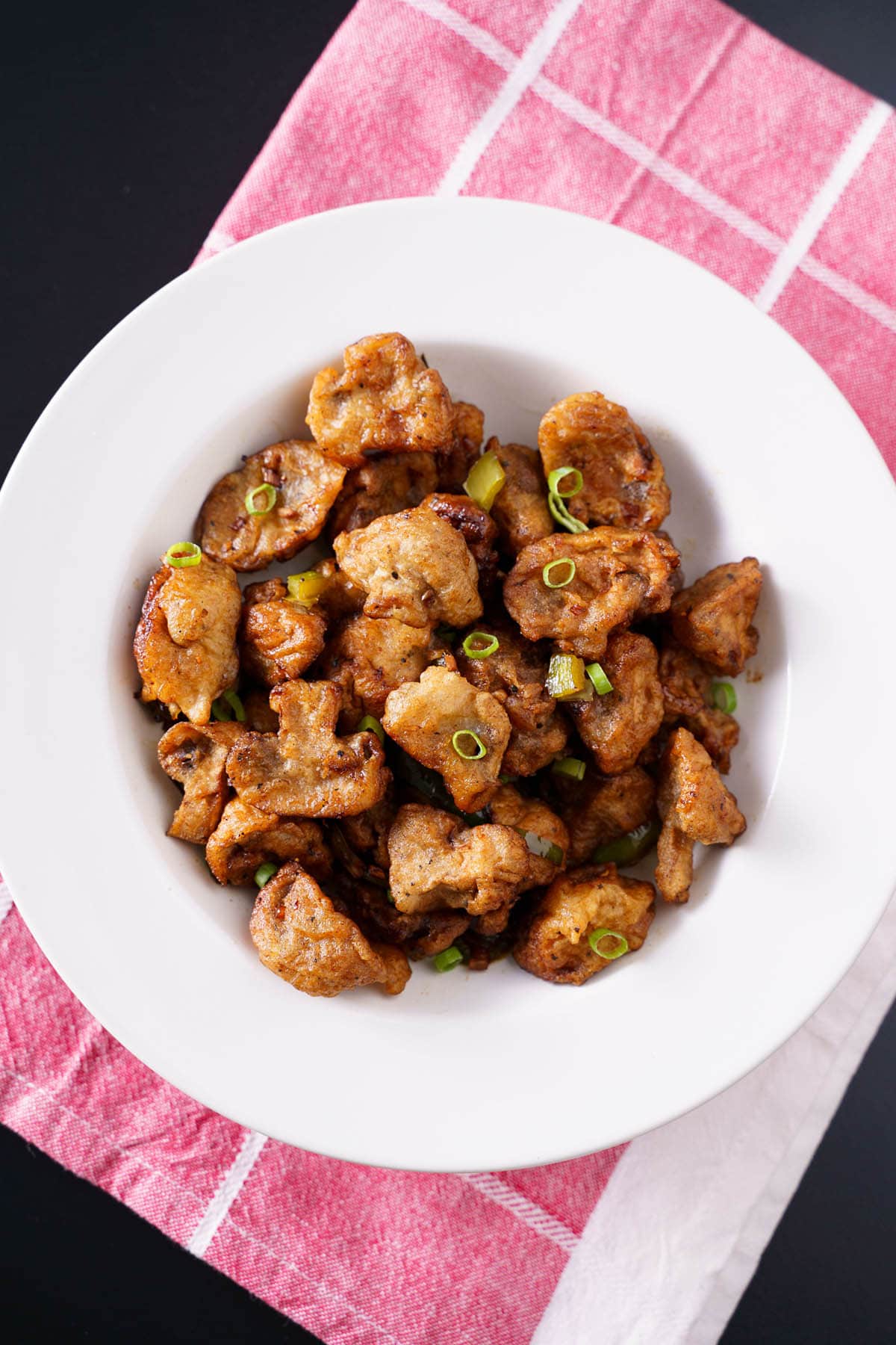 overhead shot of chilli mushroom in a shallow white bowl on a white and pink checkered napkin