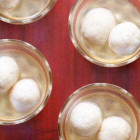 overhead shot of 4 small glass bowls with two rasgulla in sugar syrup each