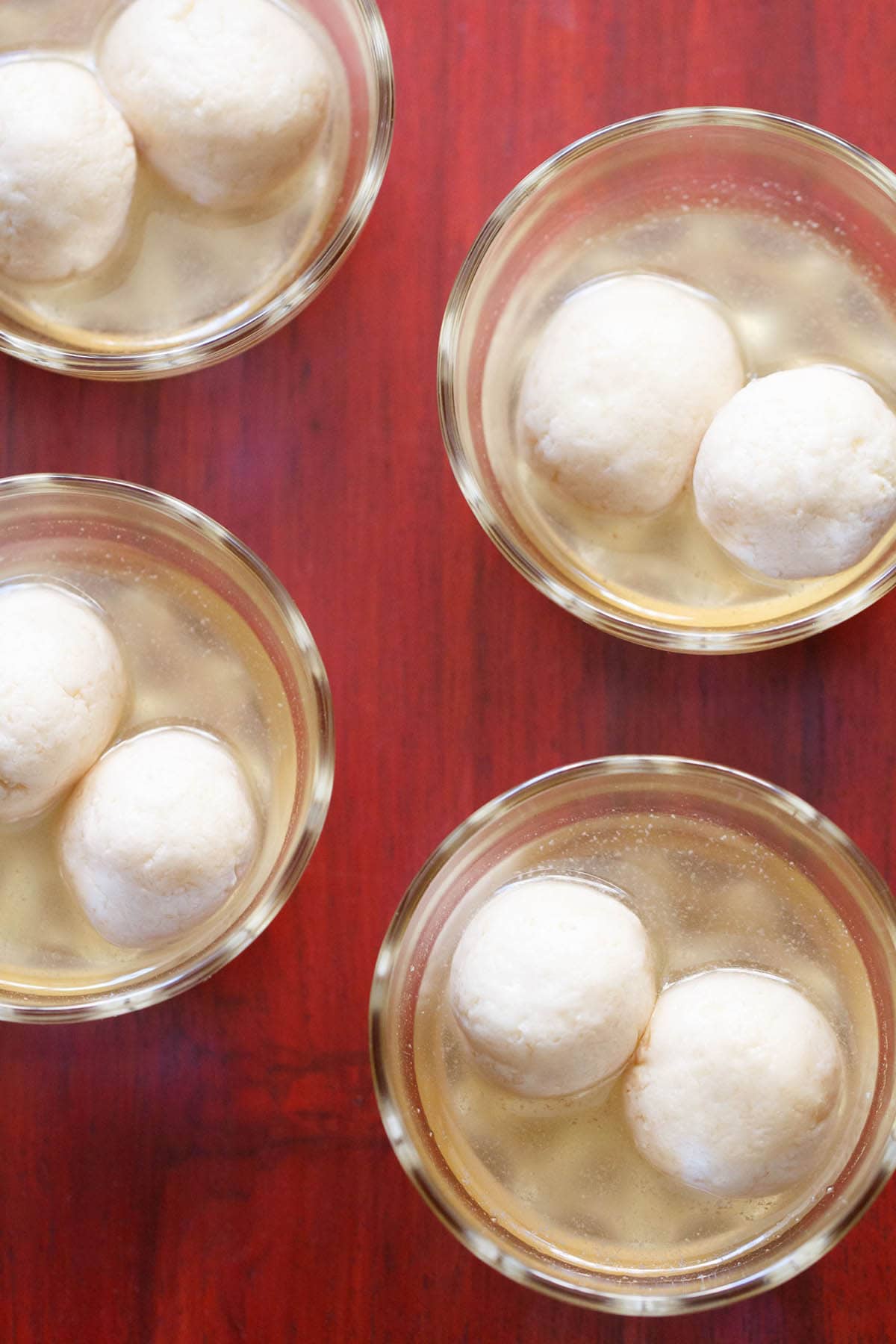 overhead shot of 4 small glass bowls with two rasgulla in sugar syrup each