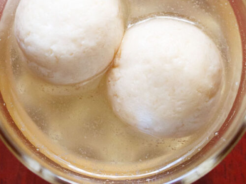 overhead shot of two rasgulla with syrup in a glass bowl