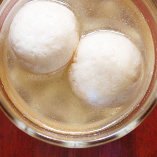 overhead shot of two rasgulla with syrup in a glass bowl