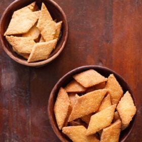 overhead shot of shankarpali, fried and baked version in two wooden bowls on a mahogany wooden board