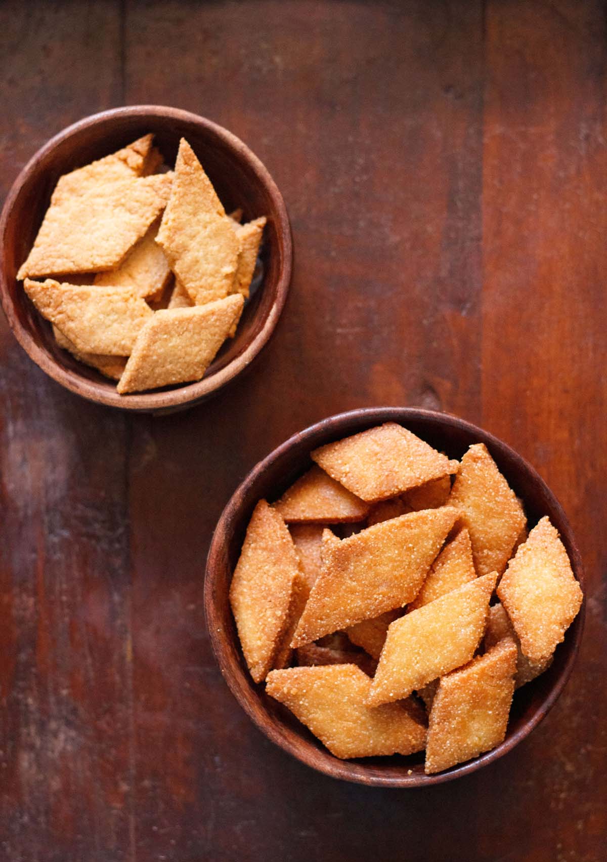 overhead shot of shankarpali, fried and baked version in two wooden bowls on a mahogany wooden board