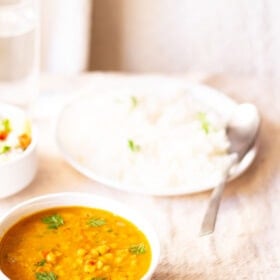 Chana dal served in a white bowl with garnish and a white plate filled with rice