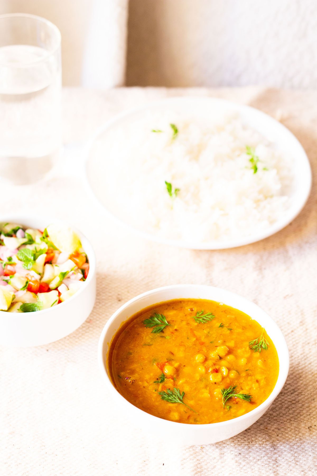 chana dal in a white bowl garnished with cilantro with a side bowl of vegetable salad and a white plate filled with rice
