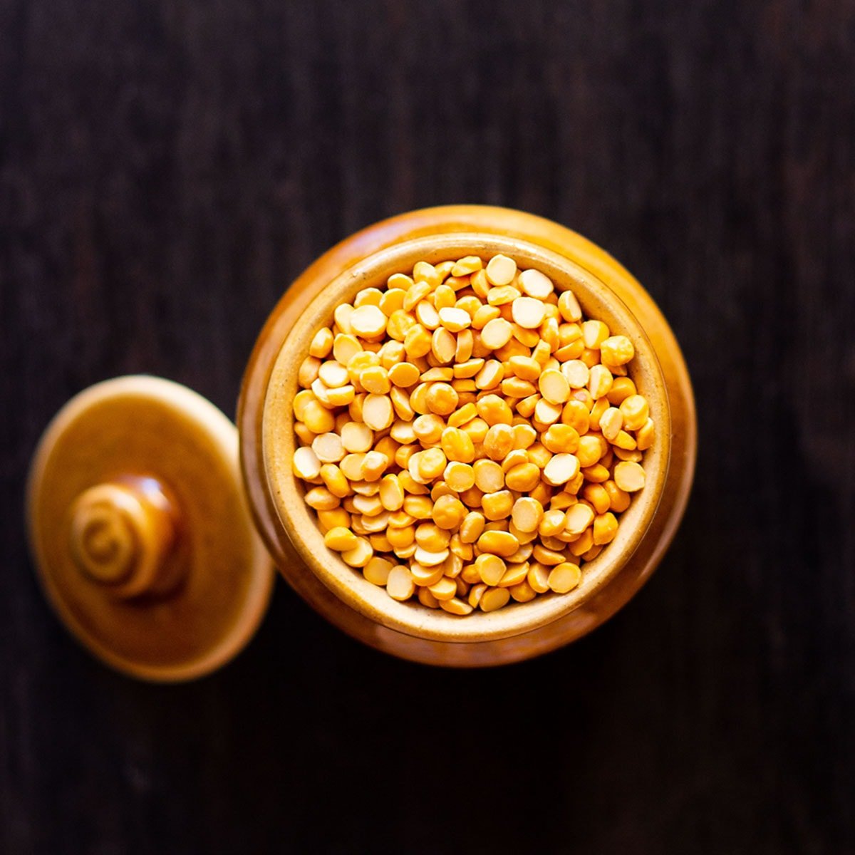 chana dal or raw hulled black chickpea lentils in a ceramic jar on a black board