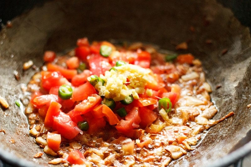 finely chopped ginger and green chilies on top of tomatoes in wok