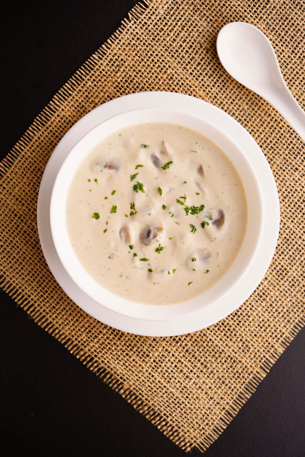 overhead shot of cream of mushroom soup in a white bowl placed on burlap