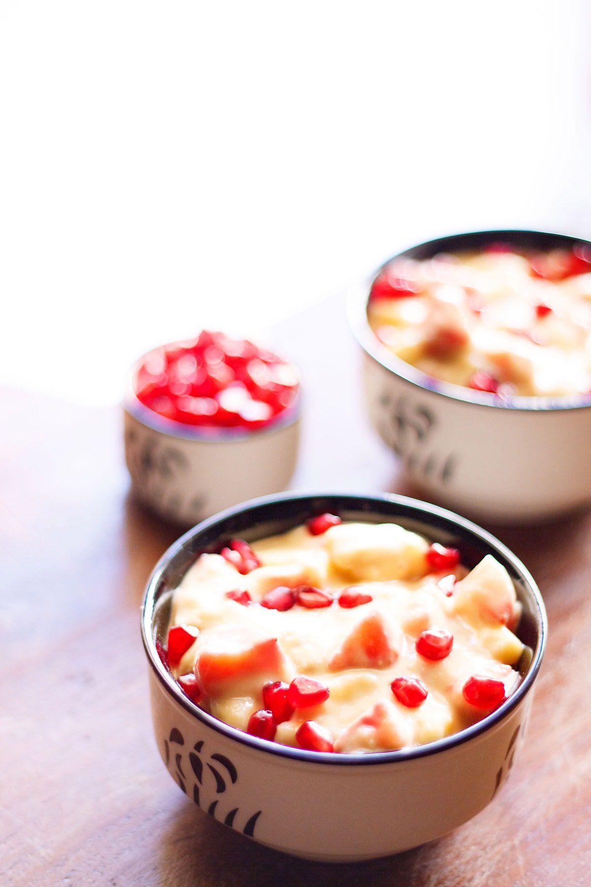 two black and white bowls filled with fruit custard and garnished with pomegranate arils