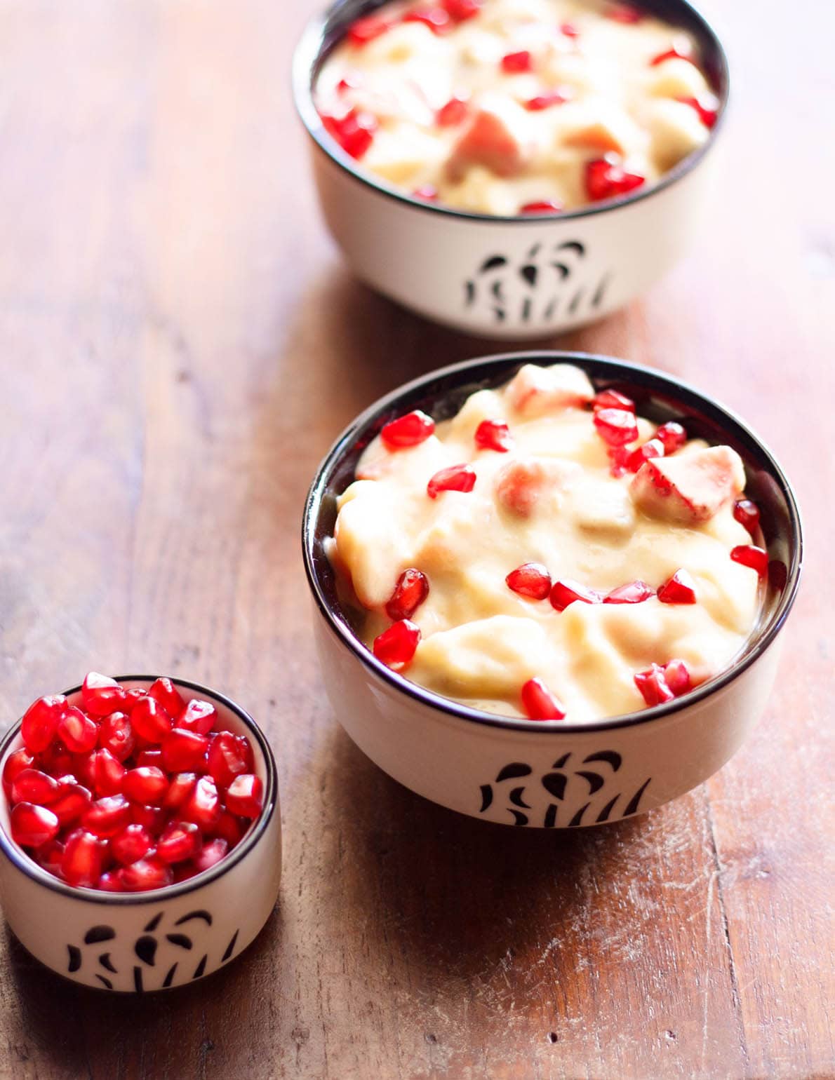 two black and white bowls filled with fruit custard and garnished with pomegranate arils