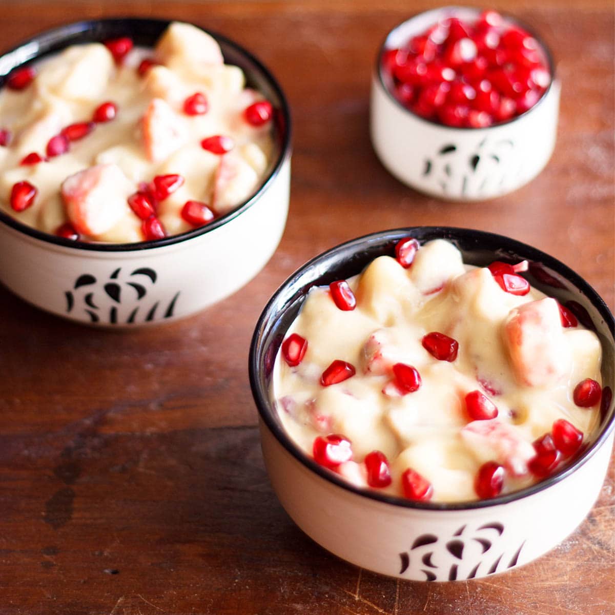 two black and white bowls filled with fruit custard and garnished with pomegranate arils