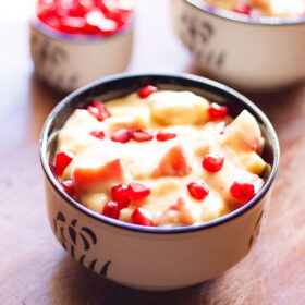 fruit custard and garnished with pomegranate arils in a black and white bowl
