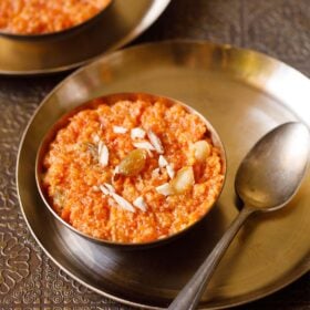 gajar ka halwa served in a bronze bowl on a bronze plate with a bronze spoon next to it