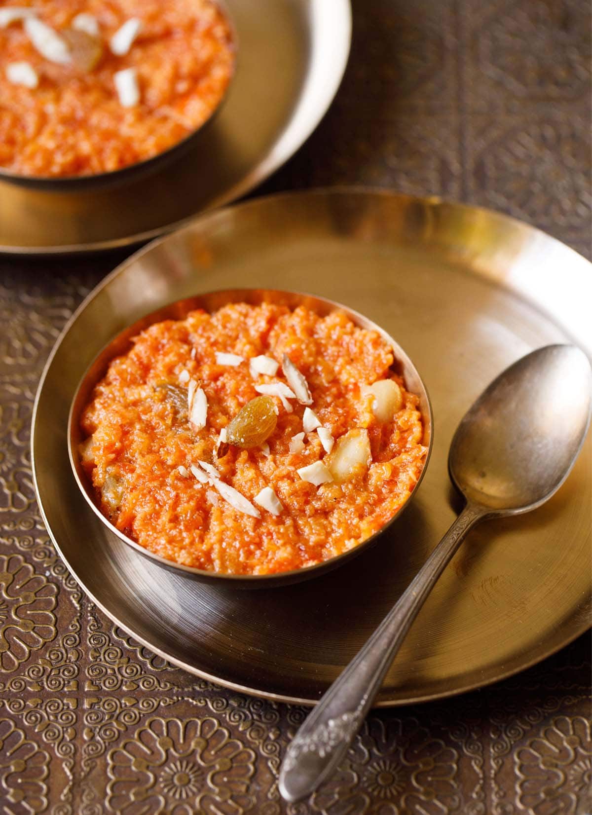 gajar ka halwa in a bronze bowl on a bronze plate with a bronze spoon by side