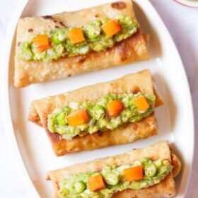 overhead shot of three chimichanga topped with guacamole and tomato cubes placed on an off-white oval tray with text layovers