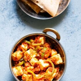 overhead shot of kadai paneer in a small kadai (Indian wok) on a light blue board