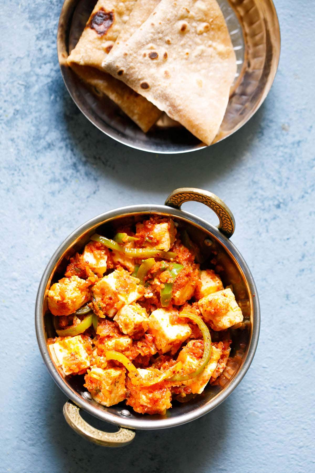 overhead shot of kadai paneer in a small kadai (Indian wok) on a light blue board