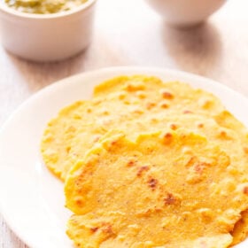 Three makki ki roti on a white plate with saag and a salad in a white bowl