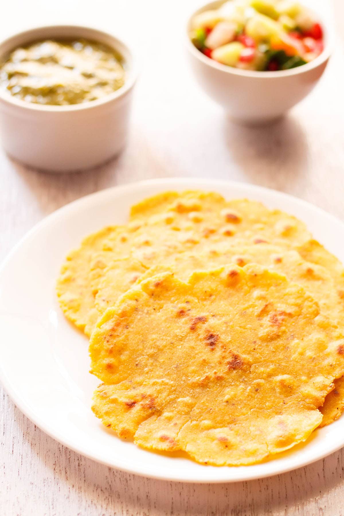 three makki ki roti in a white plate with saag and a salad in white bowls placed on top side