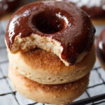 closeup shot of chocolate donut with a bite placed on top of two donuts