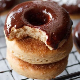 closeup shot of chocolate donut with a bite placed on top of two donuts