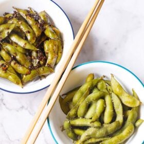 two unique edamame recipes served in two white bowls with chopsticks in the center.