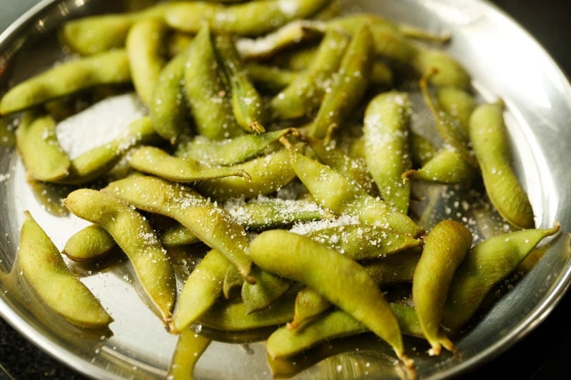 plain steamed edamame on a silver plate sprinkled with salt.