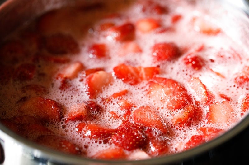 strawberry jam mixture is simmering, looking quite thin still.