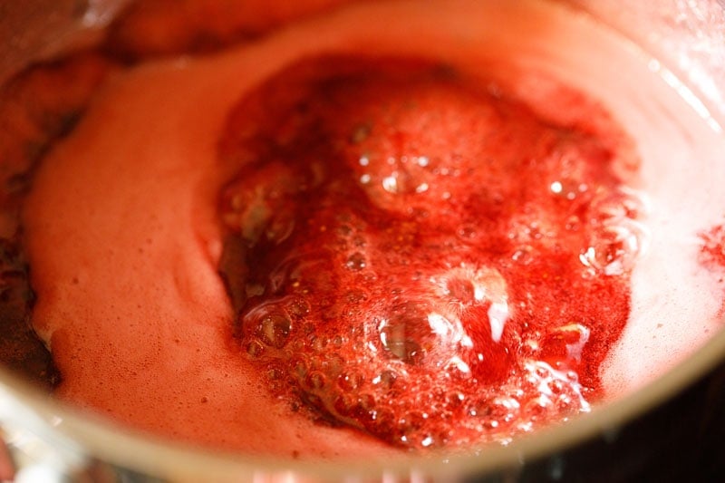 strawberry jam is continuing to simmer and become thick, with a thick coat of pink foam across the top.