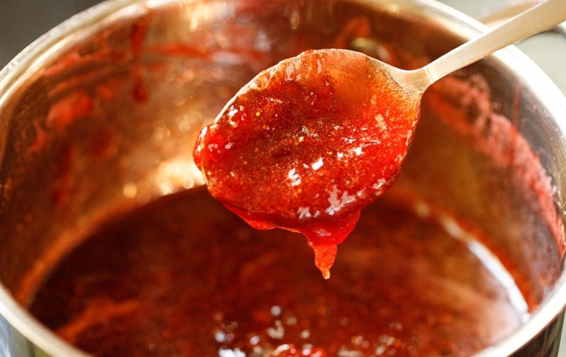 Marmeladenlöffel-Test – Erdbeermarmelade fällt in einem Blatt vom Löffel, was anzeigt, dass sie fertig ist.