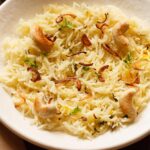 biryani rice topped with caramelized onions and cashews on an off-white plate