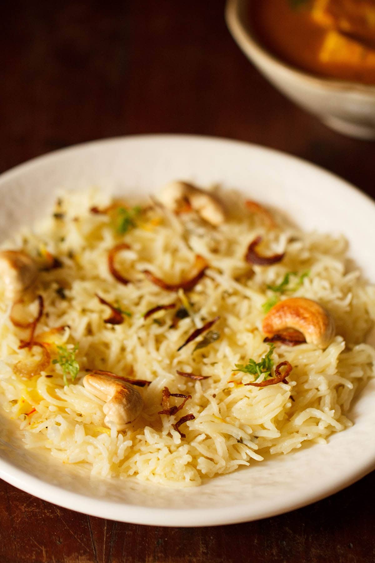 biryani rice topped with caramelized onions and cashews on an off-white plate