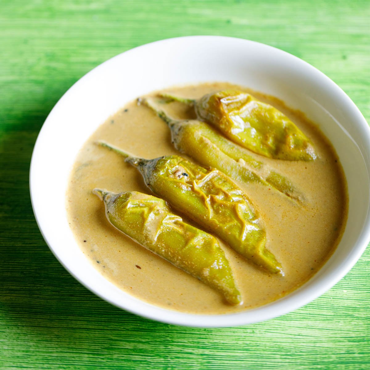 mirchi ka salan served in a white bowl on a green table.