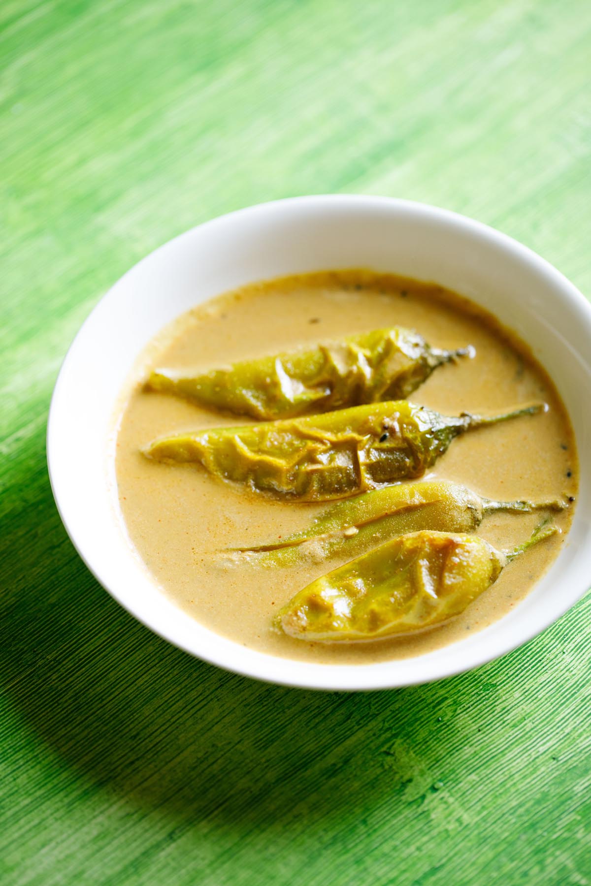 mirchi ka salan served in a white bowl on a green table.