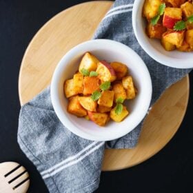 fruit salad served in two white bowls on a grey napkin on a round bamboo board