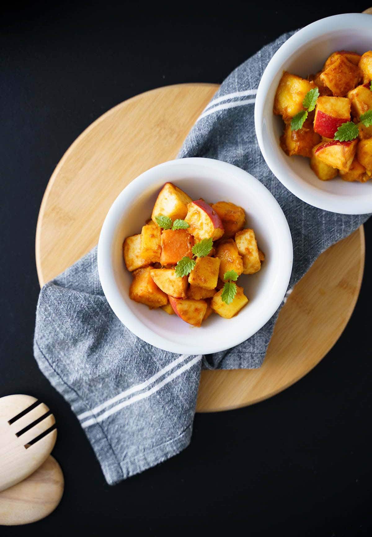 fruit salad served in two white bowls on a grey napkin on a round bamboo board