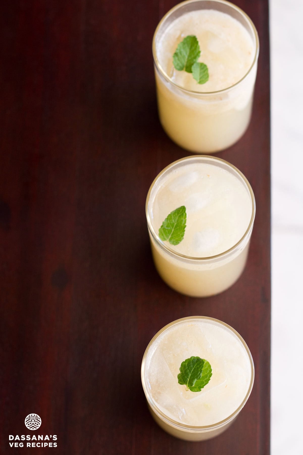 Three glasses of litchi juice placed vertically in a straight line on a wooden surface.