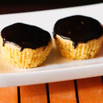 two orange muffins with chocolate glaze on top on white tray