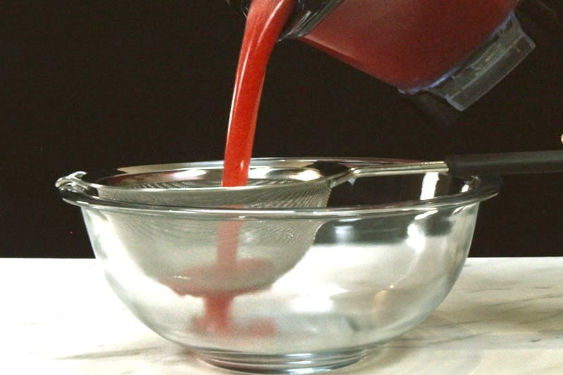 pouring agua fresca in a mesh strainer placed inside a glass bowl