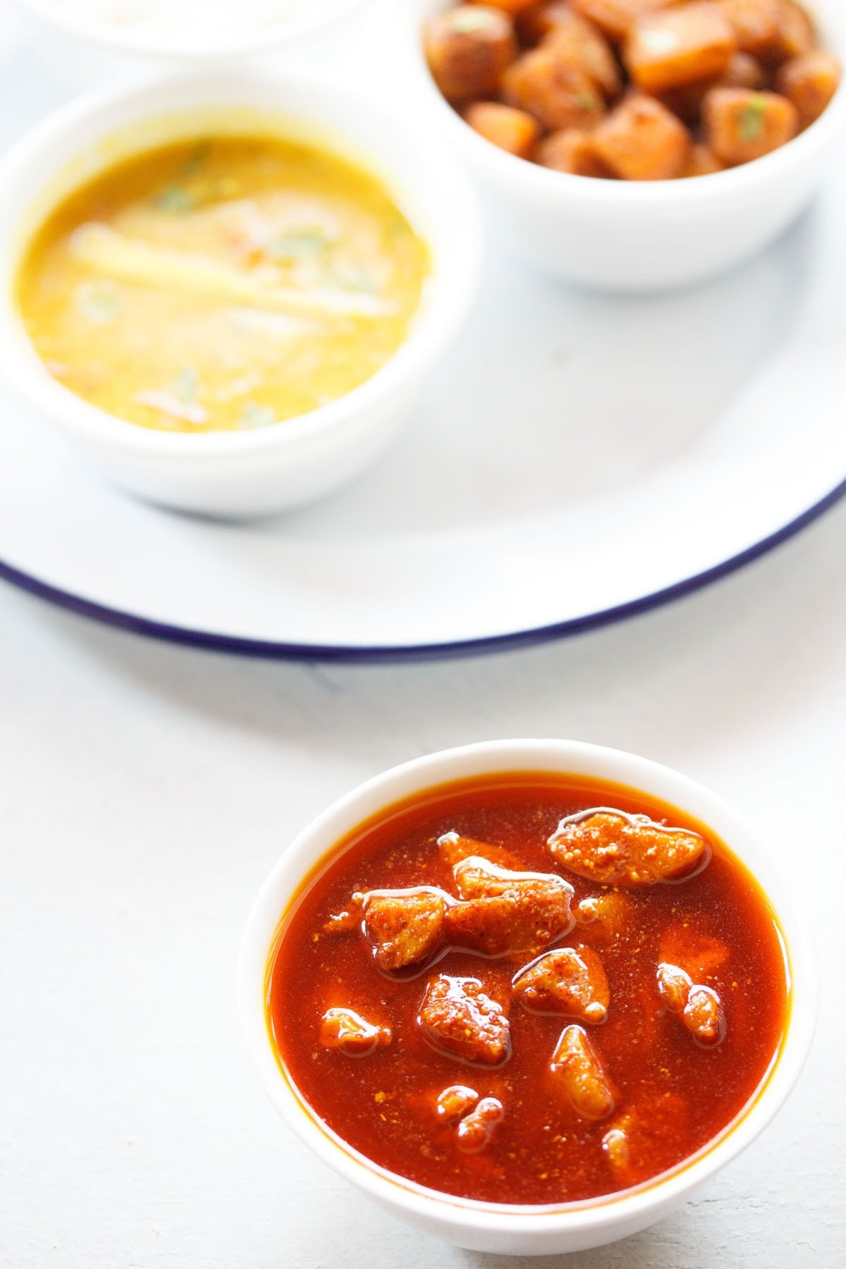 amla pickle served in a white bowl with an Indian meal on a white board.