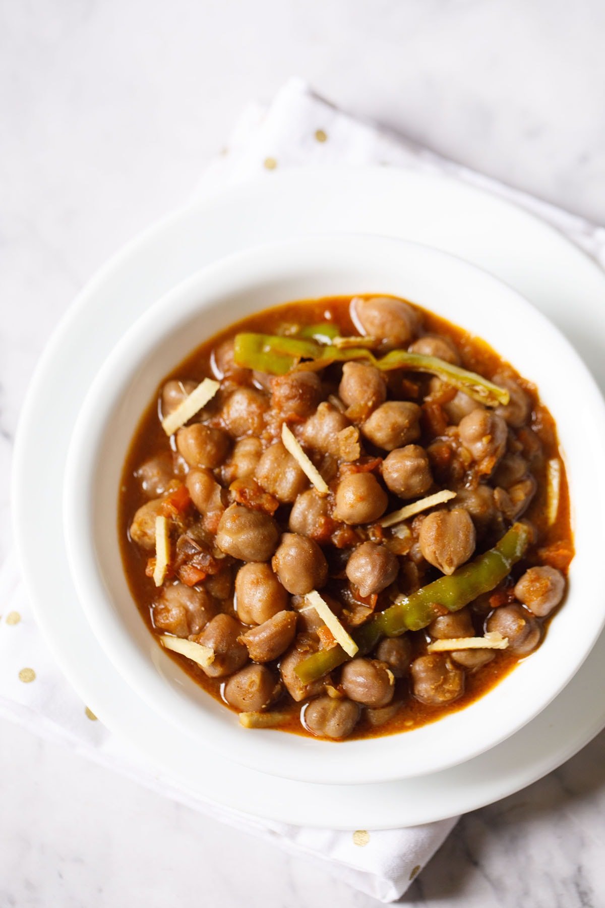 amritsari chole garnished with ginger juliennes and served in a white bowl.