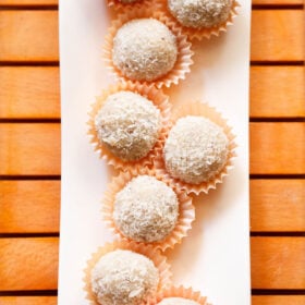 coconut ladoo in orange muffin liners on a white tray.