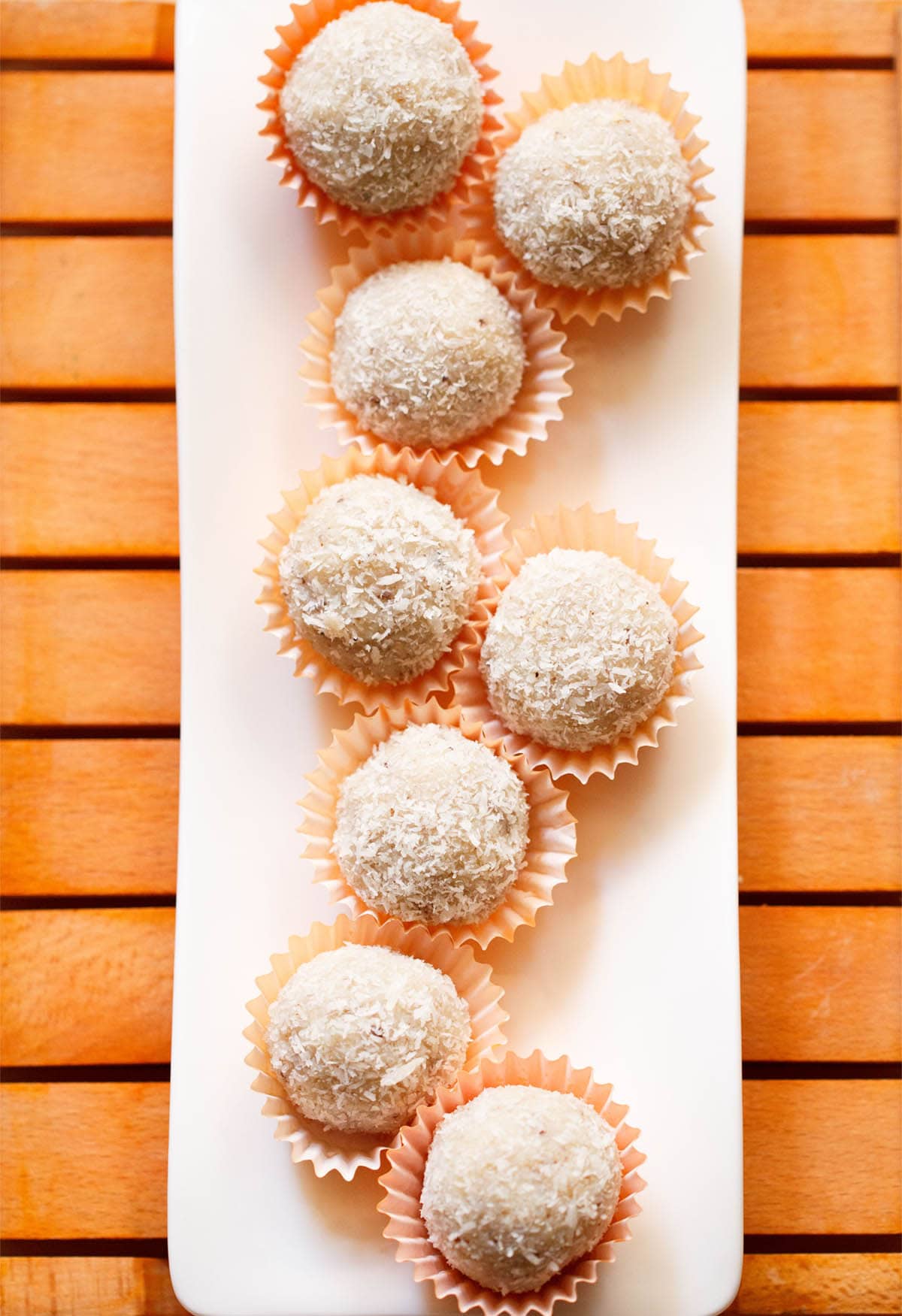 coconut ladoo in orange muffin liners on a white tray.