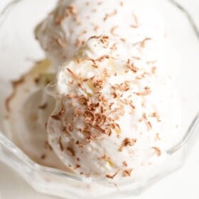 closeup shot of ice cream scoops in a glass bowl topped with grated chocolate.