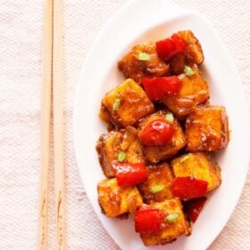 top shot of paneer manchurian on a white platter with bamboo chopsticks by the side.