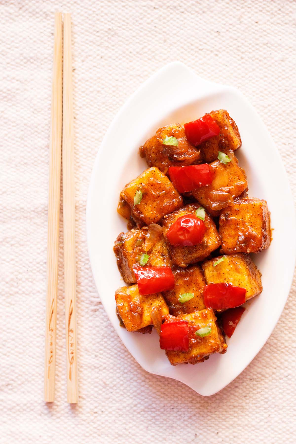 top shot of paneer manchurian on a white platter with bamboo chopsticks by the side.