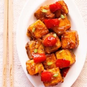 top shot of paneer manchurian on a white platter with bamboo chopsticks by the side.